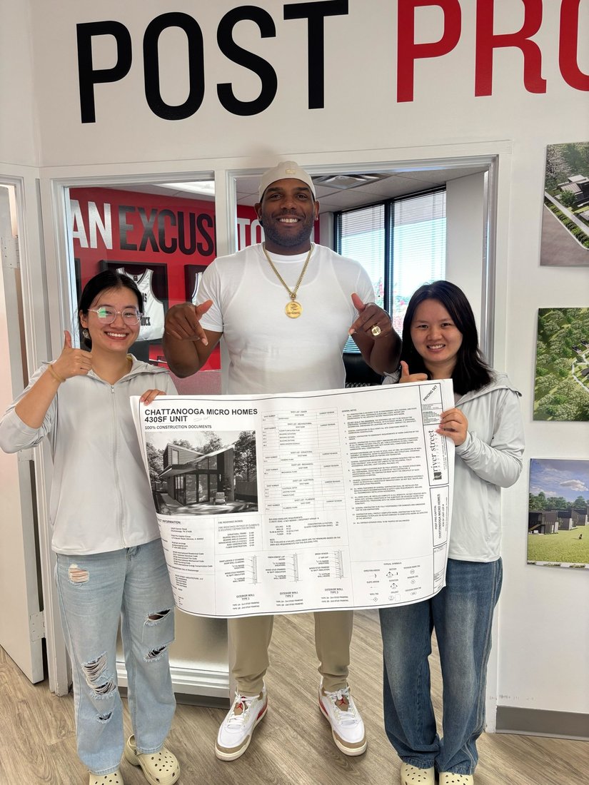 Rashad at the Post Pro Capital office holding Chattanooga Micro Homes construction plans with two team members
