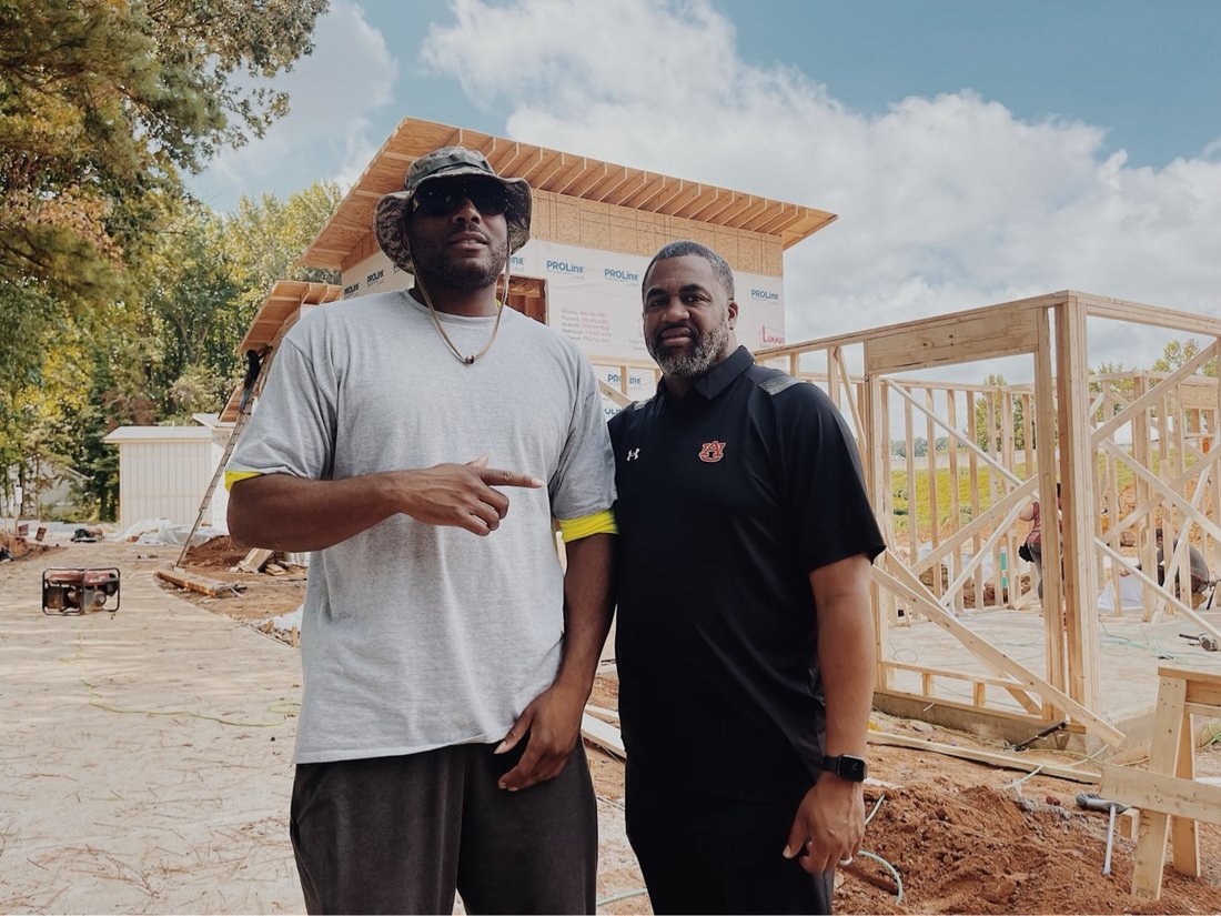 Rashad with a partner in front of framed tiny homes under construction